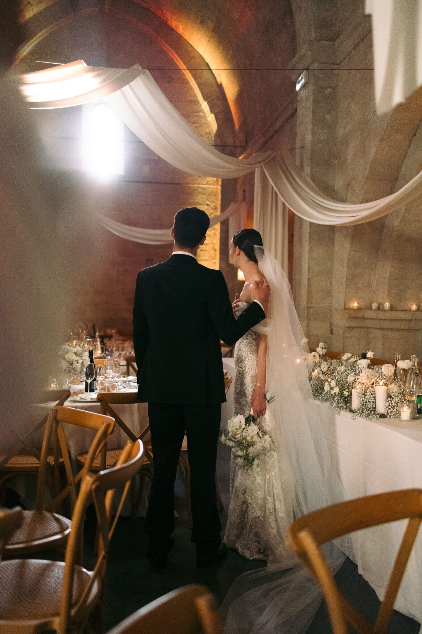 Jeune couple de mariés dans un élégant dîner de noces en Provence, décoration drapée, bouquet blanc, wedding planner présent